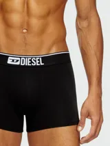 Pack de tres bóxers Diesel, uno negro con elástico blanco y logo, y dos con estampado de camuflaje en tonos grises y negros.