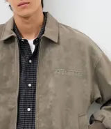 Campera de material sintético en color gris topo, con cuello inglés, cierre frontal por cremallera, mangas largas con puños elásticos y diseño de relieve tribal en la espalda.