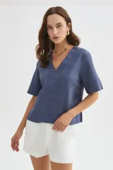 Blusa de viscosa color azul, con cuello en V, mangas cortas y detalles de costuras pespunteadas en el frente y las mangas. Presenta un diseño holgado.