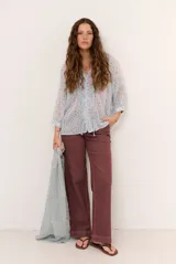 Blusa marrón semitransparente con estampado de lunares celestes, mangas largas abuchonadas, cuello en V con lazos y detalles de volados frontales.