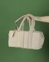 Bolso tipo tote color beige con diseño acolchado y doble asa de hombro.
