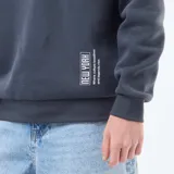 Buzo con capucha de felpa en color azul oscuro, con estampado tipográfico estilo universitario en el pecho y detalle gráfico pequeño en la parte inferior.