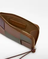 Monedero de piel con diseño de patchwork en bloques de color: marrón claro, verde oliva, marrón oscuro y borgoña. Cierre de cremallera y tirador de cuero a juego. Logo grabado en el centro.