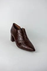 Botines de caña baja con acabado acharolado y textura efecto cocodrilo. Presentan punta fina, cierre lateral y taco cuadrado de altura media.