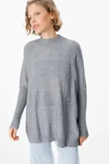 Sweater de punto gris con cuello alto, diseño holgado y mangas largas con puños acanalados extendidos hasta el codo.