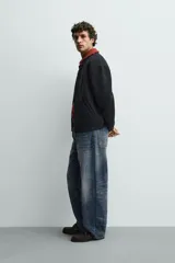 Chaqueta relaxed fit de color negro, confeccionada en tejido de canalé con mezcla de lana. Presenta cuello redondo, puños y dobladillo en rib elástico, bolsillos frontales de vivo y cierre con botones a presión.