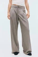 Pantalón sastre de tiro alto, color gris, con cordón ajustable en la cintura, piernas amplias con pinzas, raya marcada, bolsillos laterales discretos y bolsillos insertados atrás.