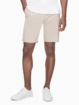 Bermuda color beige de corte recto. Confeccionada en tejido de algodón elástico. Cuenta con bolsillos laterales y traseros, cierre con cremallera y botón, trabillas para cinturón e insignia con el logo de Calvin Klein.