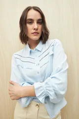 Camisa verde clara de manga larga confeccionada en viscosa ligera, con cuello clásico, cierre frontal con botones, detalles calados en la parte superior y pequeños volados.