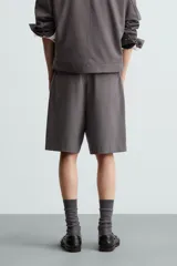 Bermuda de corte relajado color negro, con pliegues frontales, cierre de cremallera y botón, bolsillos laterales y bolsillos traseros.