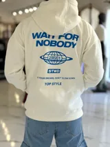 Canguro oversize blanco con capucha y bolsillo tipo canguro, confeccionado con tela de felpa suave. Presenta estampado azul en la espalda con la inscripción "WAIT FOR NOBODY", un diseño de planeta con el año 2021, el logo "STWD" y las frases "CHASE YOUR DREAMS, DON'T SLOW DOWN" y "TOP STYLE".