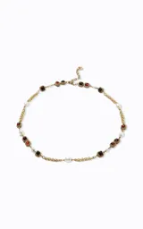 Collar largo de estilo sofisticado con cadena de metal en acabado dorado. Presenta un diseño intercalado con perlas sintéticas y detalles geométricos cuadrados con piedras en tonos rojizos y marrones.