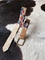 Cinto de cuero marrón claro con detalles bordados geométricos en tonos azul, rojo y beige, hebilla metálica de bronce y puntera forrada en cuero.