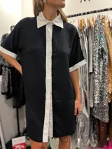 Vestido camisero corto negro con cuello, solapa y puños blancos.