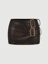 Minifalda de cuero sintético color negro, con diseño ajustado y dos correas laterales decorativas con hebillas metálicas doradas.