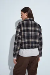 Campera de paño con diseño de cuadros en tonos negro, gris y beige. Presenta cuello camisero, cierre frontal con botones y corte corto.