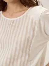 Remera de algodón con diseño combinado que presenta un panel central a rayas verticales en tonos crudo y beige, y mangas lisas en color crudo. Incluye un pequeño bordado con el número 1986 en la parte superior del pecho.