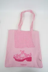 Bolso tote de tela con estampado de rayas verticales rosadas y blancas, laterales y asas en color beige. Presenta la palabra "BONJOUR" en verde en el centro y "INDIAN" en la parte inferior.