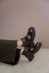 Botas de caña baja con punta cuadrada, confeccionadas en una combinación de cuero liso y gamuza en tonos marrones. Presentan un diseño con múltiples cortes y costuras visibles, cierre elástico lateral y suela de goma dentada tipo track.