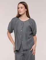 Blusa de calce relajado confeccionada en denim liviano, con cuello a la base fruncido, cierre frontal de botones metálicos y mangas cortas abullonadas con puños elastizados.