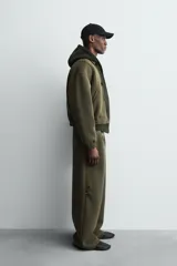 Pantalón de corte wide fit confeccionado en tejido técnico compacto con efecto neopreno. Presenta cintura elástica con cordón ajustable, pliegues frontales, bolsillos laterales y detalle de pliegues en las rodillas con aplicaciones metálicas.