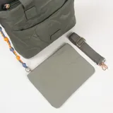 Cartera tipo tote bag color verde oliva, con diseño acolchado de formas circulares y orgánicas. Cuenta con doble asa de mano, bolsillo frontal con cierre y un detalle decorativo de cordón trenzado en colores azul y naranja. Incluye correa larga ajustable y extraíble.