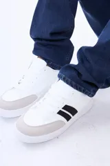 Championes urbanos de diseño moderno, color blanco con detalles en beige y franjas laterales negras. Confeccionados en cuero sintético, presentan puntera reforzada y suela de goma plana.
