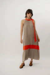 Vestido largo color tostado con cuello halter fruncido, tiras naranjas al cuello y una franja horizontal naranja en la parte inferior, de corte holgado y fluido.