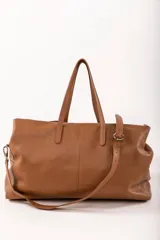 Bolso de viaje tipo weekender de cuero color marrón con doble asa de mano y correa bandolera ajustable y desmontable.