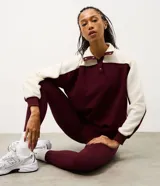 Buzo deportivo de corte oversized, con diseño bicolor en bordó y blanco. Presenta cuello alto con cierre de botones a presión, mangas largas con textura acanalada y puños elásticos.