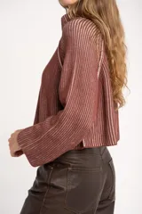 Sweater de punto acanalado color camel, con cuello alto y cierre frontal parcial. Presenta mangas largas con costuras raglán y un corte ligeramente cropped.