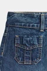 Jeans de tiro bajo y corte flare, confeccionados en denim azul con lavado localizado. Presentan bolsillos de plastrón en el delantero, trabillas para cinturón y cierre frontal con cremallera y doble botón metálico.