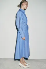 Vestido midi de corte camisero con estampado de rayas verticales, cuello solapa, manga larga con puños y cierre frontal con botones. Incluye un cinturón de lazada en el mismo tejido y bolsillos laterales ocultos.
