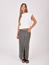 Falda larga de denim color gris oscuro, con diseño cruzado frontal (wrap) que se ajusta con botones plateados, creando una abertura pronunciada.