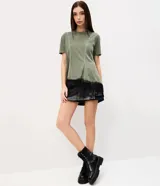 Remera verde militar de algodón con efecto desteñido, cuello redondo, mangas cortas, recortes asimétricos y detalle de encaje negro en el bajo irregular.