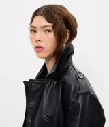 Campera de cuero sintético estilo trench, con cuello solapa, cierre frontal de botones y lazo ajustable en la cintura. Presenta detalles utilitarios en hombros y puños.