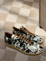 Zapatillas bajas con estampado animal print de vaca en blanco y negro, con cordones marrones y suela color caramelo.