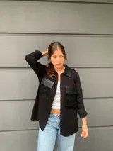 Camisa negra de tejido de punto con cuello clásico, cierre frontal con botones y dos bolsillos de cuero en el pecho.