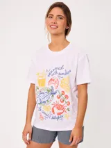 Remera blanca de manga corta y corte holgado, con estampa frontal multicolor de estilo veraniego con ilustraciones de alimentos y textos.
