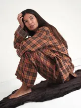 Pijama de dos piezas a cuadros color naranja y negro con ribetes rosas. La camisa es de manga larga con cuello y puños marrones. El pantalón es de corte recto.