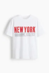 Remera blanca de manga corta y cuello redondo, con estampado frontal que dice "NEW YORK" en rojo y "ATHLETICS" en contorno negro, acompañado de un texto pequeño.