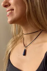 Gargantilla de cuero negro con dije de piedra blanca en forma de lágrima con engarce dorado.