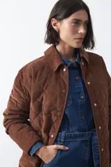 Campera capitoneada de algodón con diseño matelaseado, cuello camisero y cierre frontal con botones a presión. Presenta un corte relajado y bolsillos frontales.