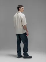 Camisa de manga corta color blanco roto, con cuello clásico y cierre frontal de botones.