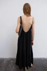 Vestido midi de color negro, confeccionado en tejido fluido, con escote en V y tirantes finos ajustables. Presenta frunces en el pecho y un volante en el bajo.