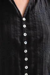 Blusa negra de manga larga con cierre frontal de botones, cuello mao y textura sutilmente rayada con detalles bordados.