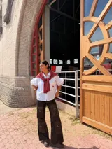 Camisa blanca de corte holgado y diseño amplio, con cuello clásico, mangas largas y un bolsillo frontal en el pecho adornado con un bordado rojo.