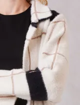 Chaqueta de tejido suave con estampado a cuadros en tonos beige y blanco, cuello con solapa y cierre de botón frontal. Incluye bolsillos delanteros.