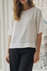 Blusa de corte oversize en color blanco, con cuello redondo y mangas cortas de estilo holgado. Confeccionada en tejido ligero con textura sutil.
