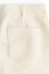 Pantalón amplio color crudo confeccionado en punto bouclé, con elástico oculto en la cintura, cierre decorativo con botón, bolsillos delanteros y bolsillos de parche en la parte trasera.